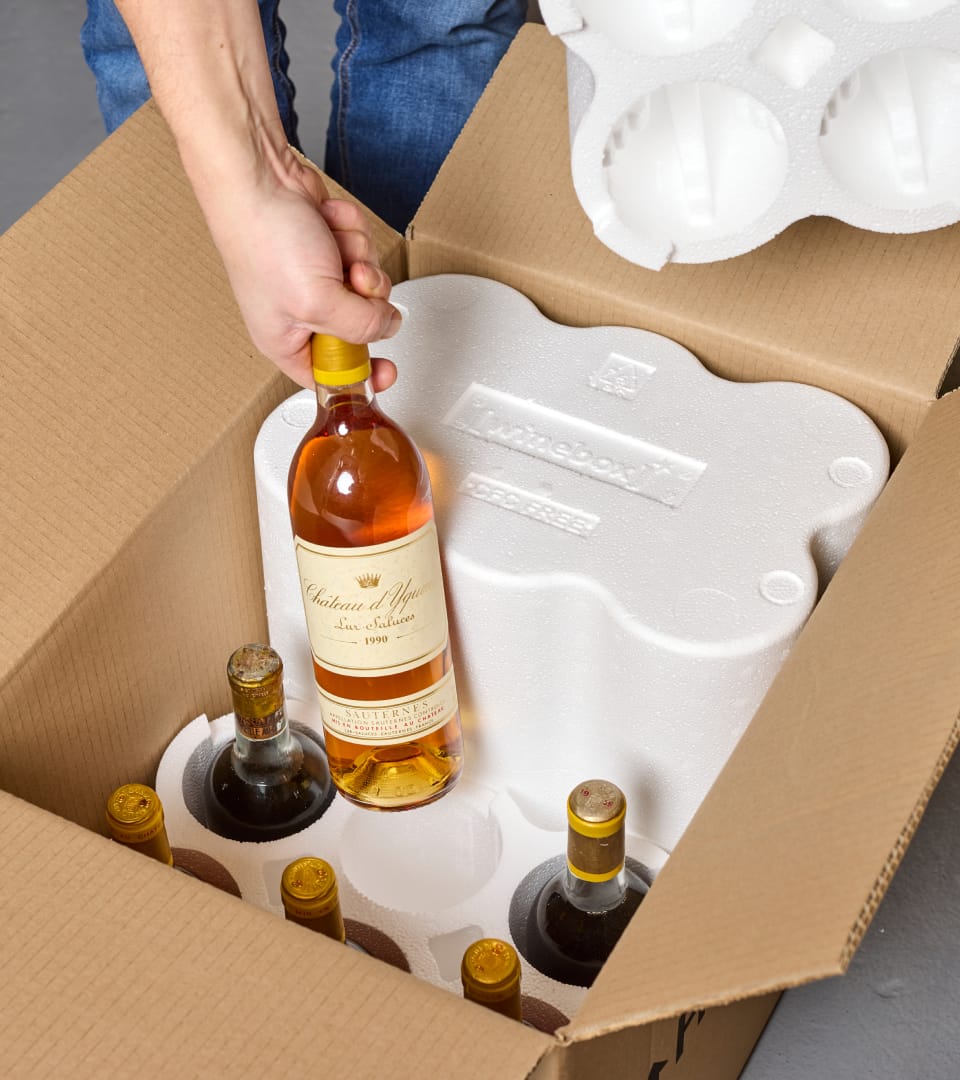 A person adding a bottle of wine to a packaging box
