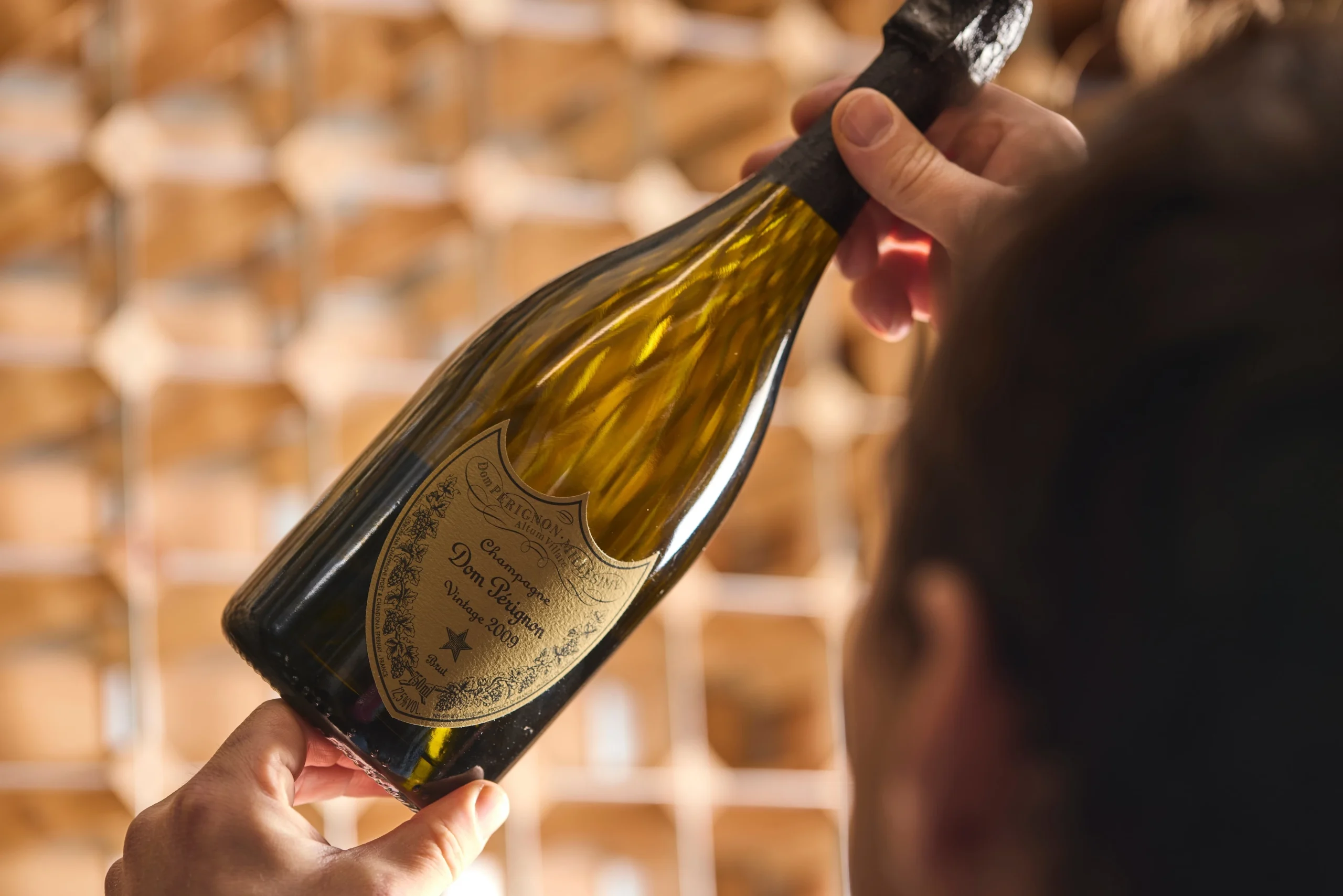 A person holding up a bottle of Dom Perignon champagne to the light for inspection